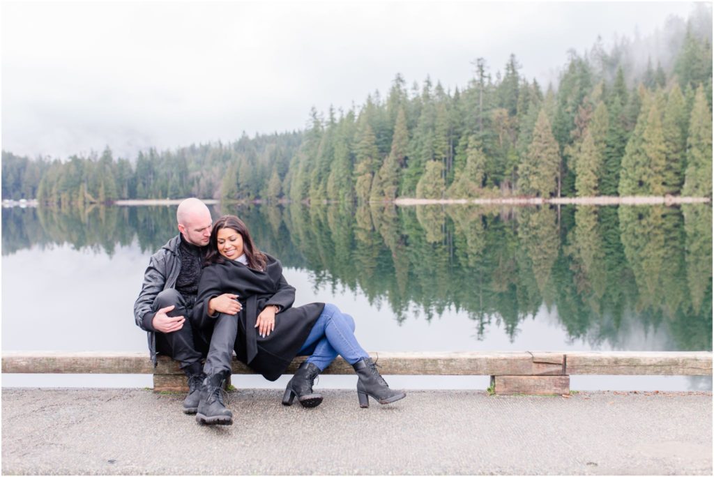 Engaged couple sitting by the lakeside at Sasamat Lake in Port Moody